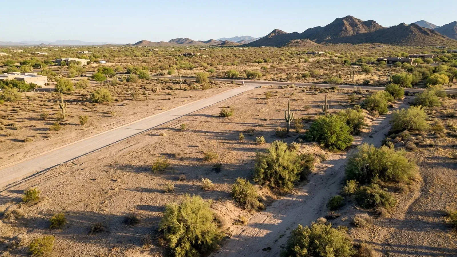 Aerial view of an undeveloped desert lot with creosote, palo verde and saguaro, a dirt access road and a dry wash across one corner.